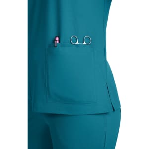 A teal scrub top featuring a pocket with a pen and scissors visible, alongside a branded logo.