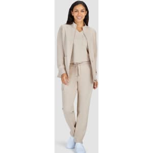 A woman is wearing a beige jacket and matching pants, paired with a simple top and white shoes. The outfit is stylish and modern.