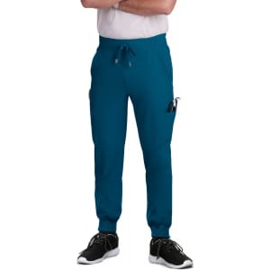A pair of teal joggers featuring pockets and an elastic waistband, displayed on a standing model wearing black shoes.