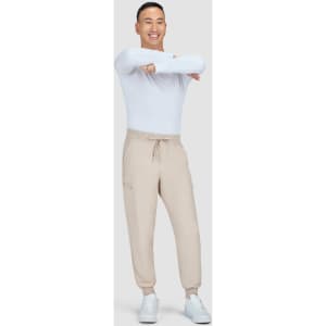A model wearing beige joggers and a white long-sleeve shirt, smiling and posing against a plain background.