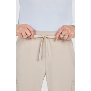 A close-up of a person’s hands tying the drawstring of beige jogger pants. The pants feature a casual design and waistband.