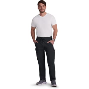A man wearing black Neuro Cargo Pants and a white t-shirt, standing with hands in pockets. The pants have a logo.