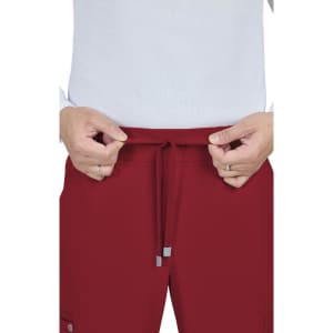 A person wearing red cargo pants, adjusting the waistband with both hands, featuring a tie and pockets.