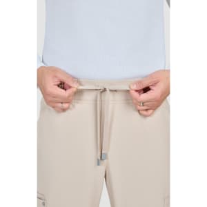 Beige Neuro Cargo Pants feature a drawstring waist and side pockets, with a person adjusting the waistband.