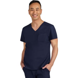 A navy blue scrubs top featuring a V-neck and a chest pocket. The model is smiling and wearing matching scrubs pants.