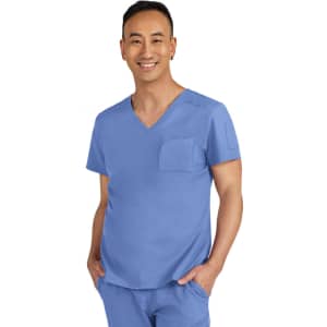 A man wearing a blue scrub top with a pocket, smiling at the camera. The outfit includes short sleeves and a v-neck.