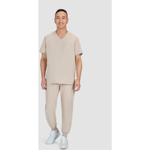 A model wearing beige scrubs with a v-neck top and jogger-style pants, paired with white sneakers.