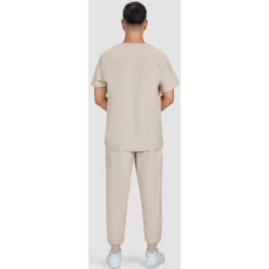 A man stands with his back to the camera, wearing a beige medical uniform consisting of a short-sleeve top and pants.