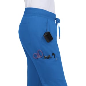Scrub pants in blue with pockets containing scissors and a black device, showing a casual fit and elastic waistband.