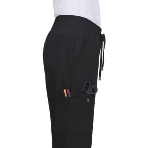 Black Atria Pant featuring pockets, including one with tools such as scissors and pens. Includes a logo on the fabric.