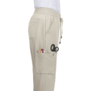 A beige Atria Pant featuring side pockets, one with scissors and pens, and a drawstring waist.