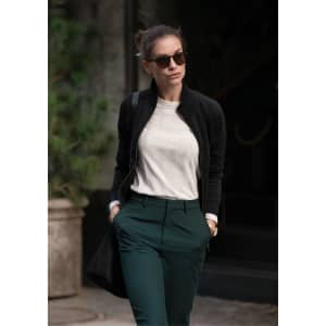 A stylish black women's jacket worn over a light-coloured top, paired with dark green trousers and sunglasses.
