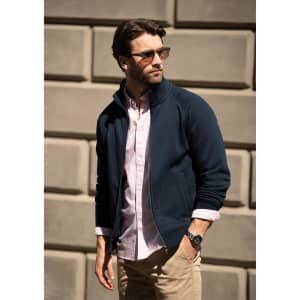 A navy jacket worn over a light pink shirt, modelled by a man with sunglasses against a textured wall.