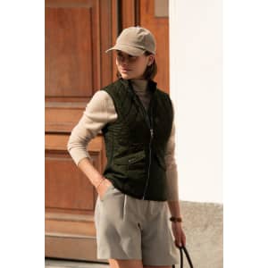 A green women's vest with a quilted pattern, worn over a beige top, paired with light grey shorts and a cap.