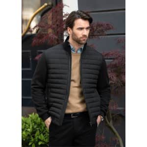 A black puffer jacket worn by a man, featuring a zip closure and standing outdoors against a backdrop of greenery.