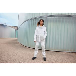 A model wearing a white and grey hardshell rainjacket with a hood, paired with matching pants and black shoes.