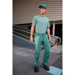 A man wearing all-season workwear pants in a shade of green, paired with a matching cap and shirt.