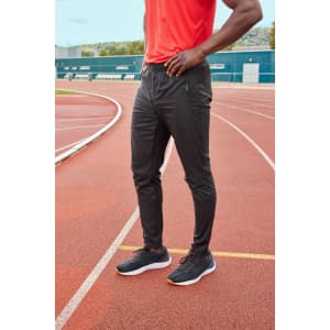 Men's running pants in black, styled with a red top, worn on a running track. Featuring a logo on the pants.