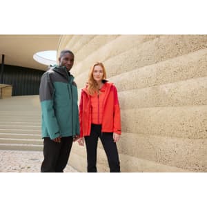 A red and grey women's 3-in-1 jacket and a teal and grey men's jacket displayed against a textured wall. Both feature logos.