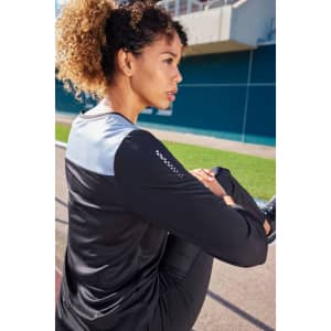 A long-sleeve ladies' running shirt in black and grey, featuring a logo, displayed on a model outdoors.