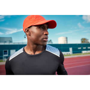 A long-sleeve men's running shirt in black with light grey accents, worn by a man in an orange cap.