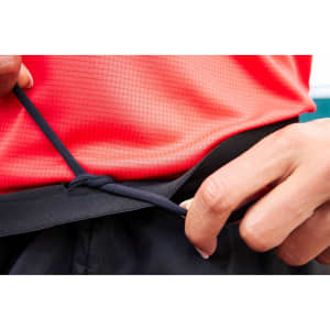 A hand adjusts the drawstring of black ladies running shorts, paired with a red top in a sporty setting.