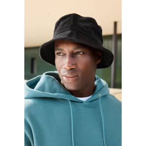 A black corduroy fisherman hat sits atop a model wearing a green hoodie, displayed against an outdoor background.