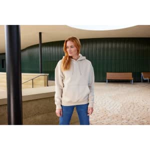 An oversized unisex sweatshirt in beige, featuring a hood, worn with blue jeans in an outdoor setting.