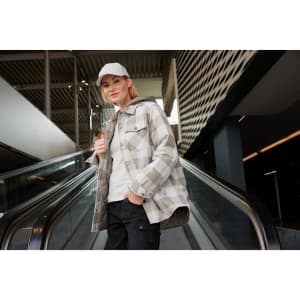 A check shirt jacket in grey tones, featuring a hood, worn by a model in a modern indoor setting.