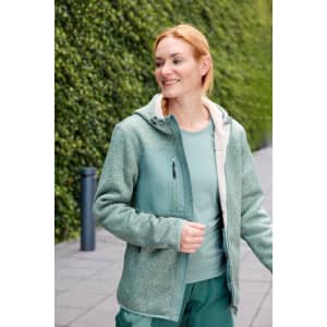 A green knitted fleece jacket with a zip and hood, worn by a smiling person outdoors amidst greenery.