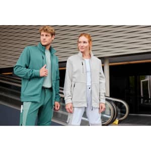 A green fleece jacket and a light grey fleece jacket on a man and a woman, with a building backdrop. Both jackets have zippers and pockets.