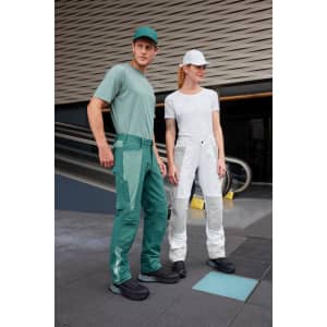 A model wears green work pants and another model wears white work pants, both paired with casual tops and caps.