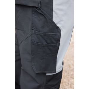 A close-up of a dark grey workwear softshell jacket featuring multiple pockets and a contrasting light grey side panel.