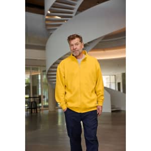 A man wearing a yellow sweat jacket walks through a bright, modern space with a spiral staircase in the background.