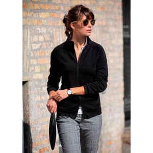 A black jacket worn by a woman, paired with sunglasses and stylish trousers, standing against a brick wall.