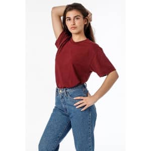 A woman poses in a maroon short sleeve cotton poly crew tee, paired with high-waisted blue jeans. The tee has a logo.