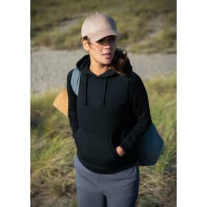 A black hoodie worn by a woman, paired with a cap, standing outdoors with grass in the background.
