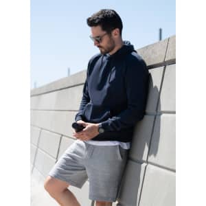 A navy hoodie with a branded logo, worn by a man leaning against a wall, paired with grey shorts.