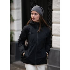 A black women's jacket with a hood, paired with a grey beanie, set against an urban backdrop.