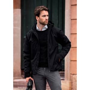 A black puffer jacket features a hood, worn over a black sweater, paired with light grey pants and a bag.