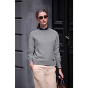 A woman wearing a grey sweatshirt and beige pants, accessorised with sunglasses and carrying a brown bag.