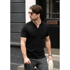 A man in a black V-neck polo shirt and sunglasses walking outside, carrying a bag and a hat.