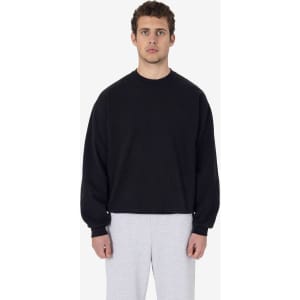 A black heavy fleece pullover sweater worn by a model, paired with light grey bottoms. It features a logo.