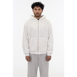 A heavy fleece zip-up hoodie in cream, featuring a hood and a front zipper. The model wears grey pants.
