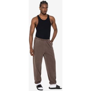 A model wears heavy fleece sweatpants in brown, paired with a black tank top and sandals. The pants have a logo.