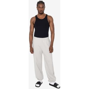 A man wearing a black tank top and light grey heavy fleece sweatpants, styled with sandals. The sweatpants have a logo.