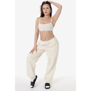 A model wearing cream-coloured heavy fleece sweatpants with a fitted top and slides, striking a casual pose.