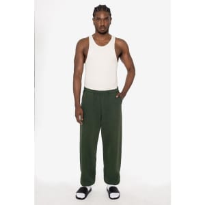 A man stands in a tank top and dark green heavy fleece sweatpants, with one hand in a pocket. The pants have a logo.