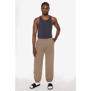 A model wearing a fitted black tank top and beige track pants, paired with sandals. The pants feature a relaxed fit.
