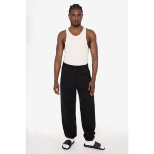 A model wearing black heavy fleece sweatpants with a white tank top and black sandals, featuring a logo.